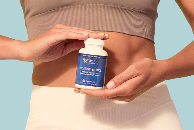 Woman holding blue supplement bottle in front of abdomen, light blue background.