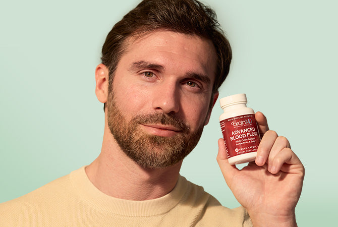 Bearded man holding a red supplement bottle against a light green background.