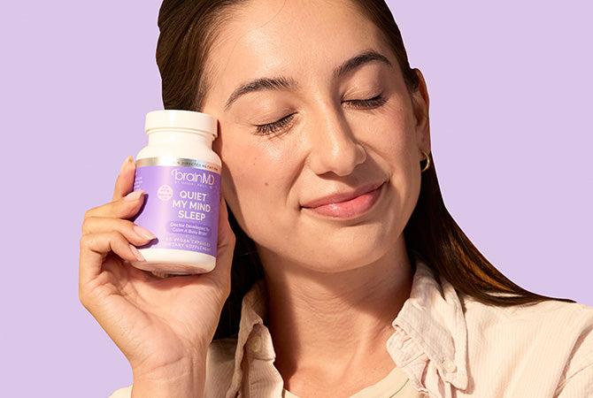 Woman holding a purple supplement bottle next to her face in front of a lavender background.