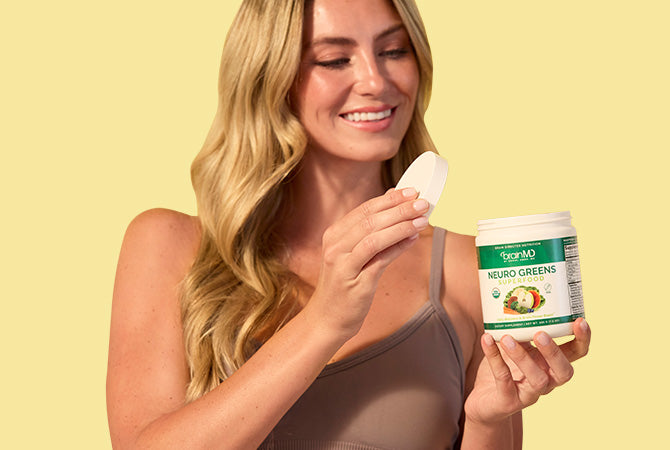 Smiling woman taking lid off a green supplement container, yellow background.