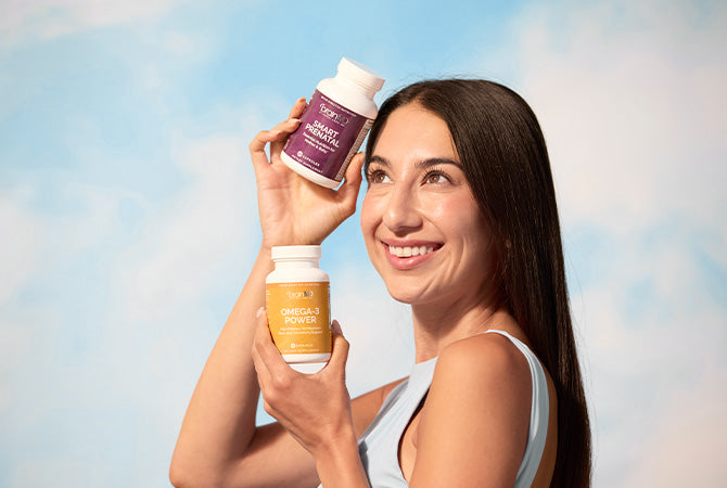 Smiling woman holding 2 supplement bottles against a sky background.