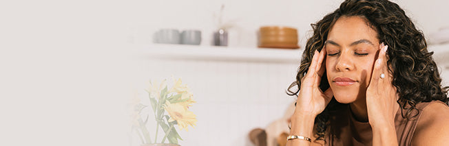 Woman holding her temples in front of a white interior background, horizontal panel.