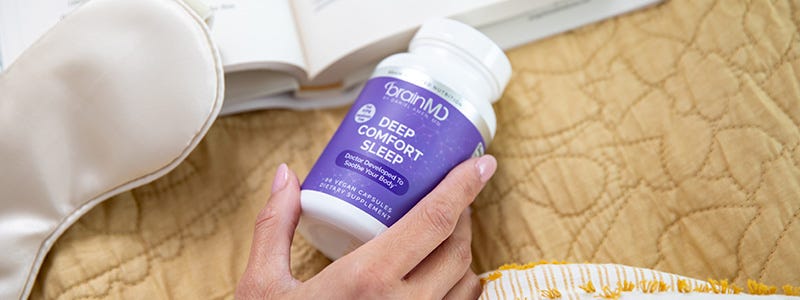 Hand holding purple supplement bottle on top of a yellow bed cover, rectangular shape.