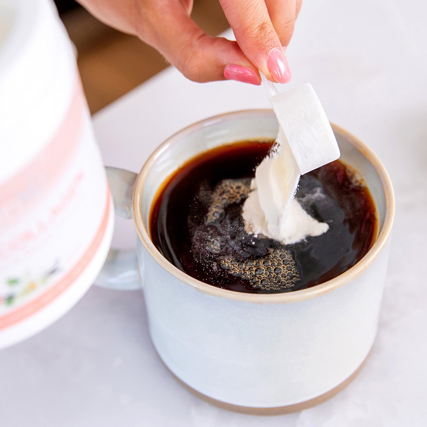 BrainMD Smart Collagen: woman pouring a scoop of powder into a mug of dark liquid