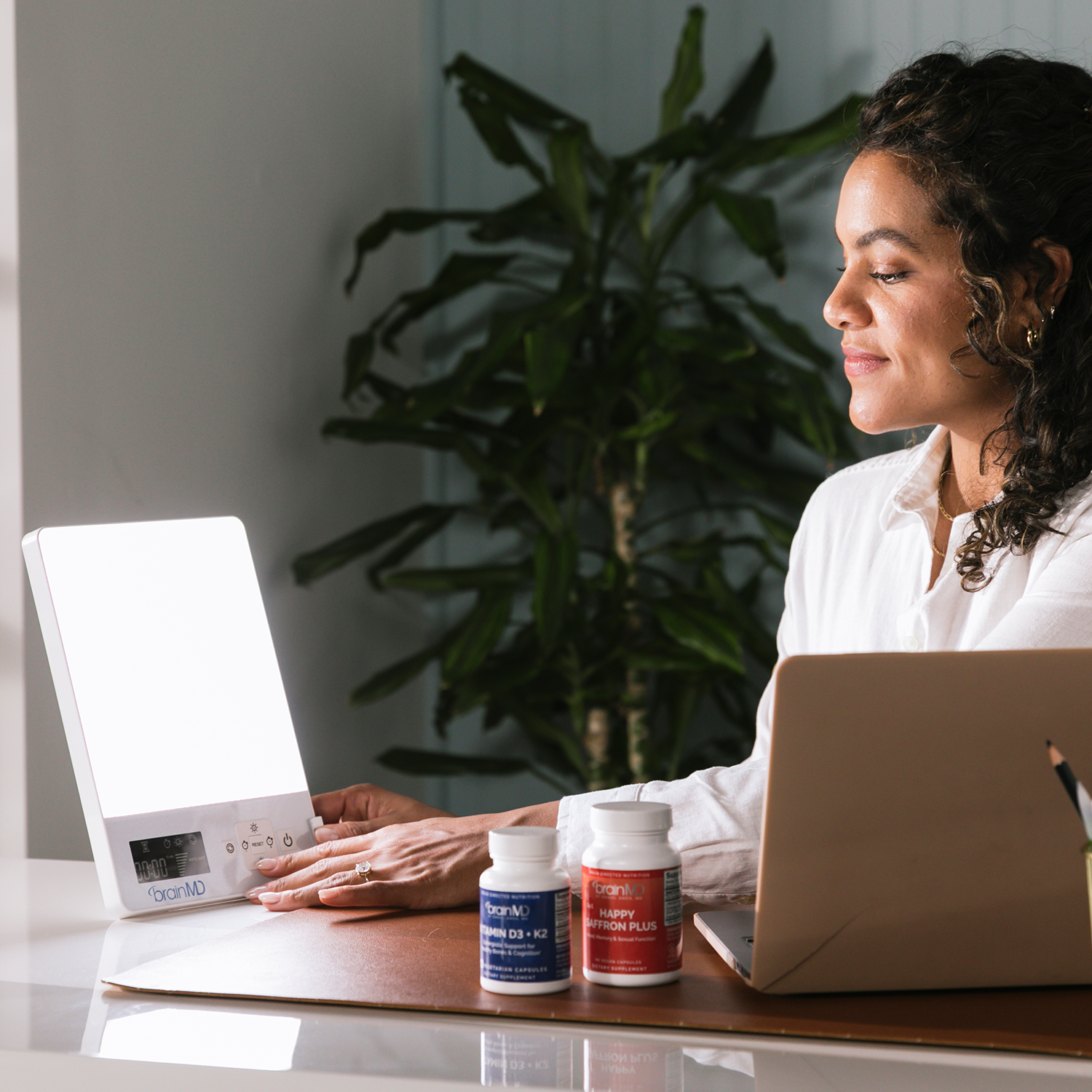 Woman in office basking in the glow of the BRIGHT MINDS Therapy Lamp...side view.
