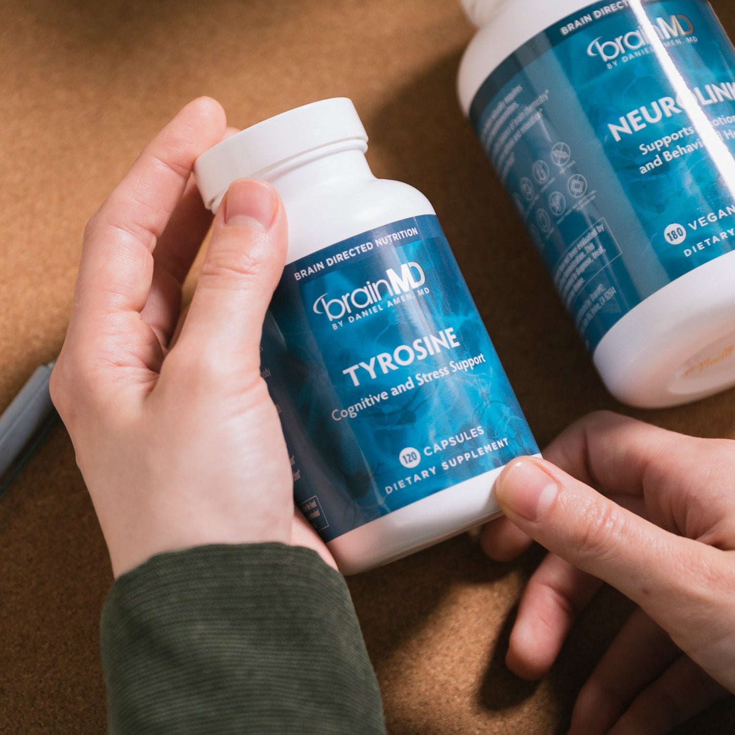 BrainMD Tyrosine: person holds blue supplement bottle against a brown background