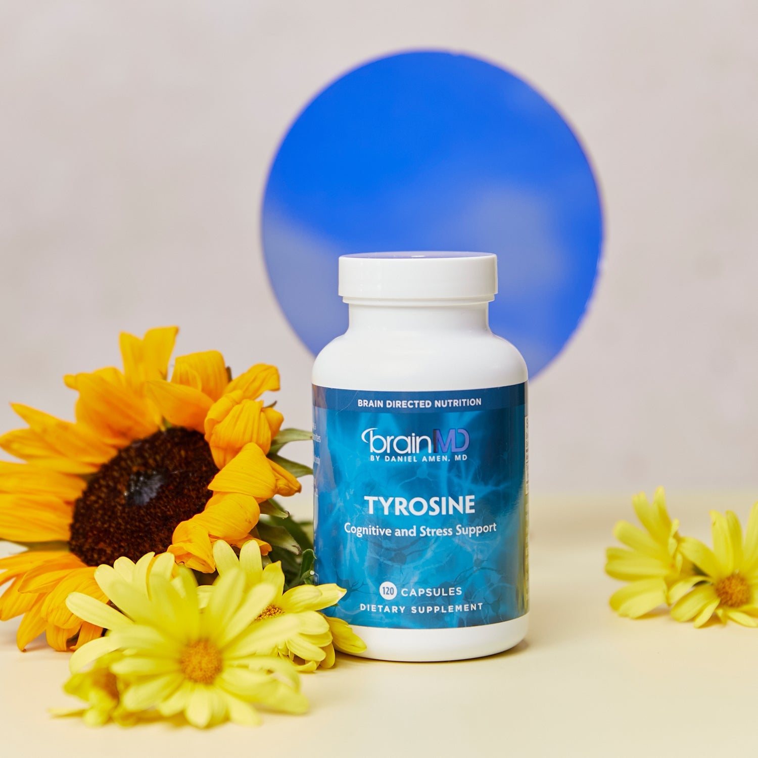 BrainMD Tyrosine: stress support supplement, blue dot in the background with yellow flowers flanking the bottle