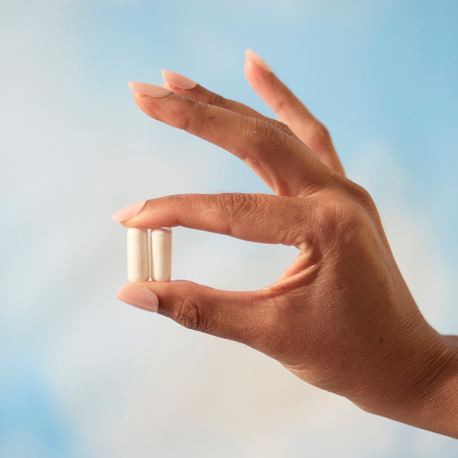 BrainMD Tyrosine: stress support supplement, woman holding two capsules against a sky background