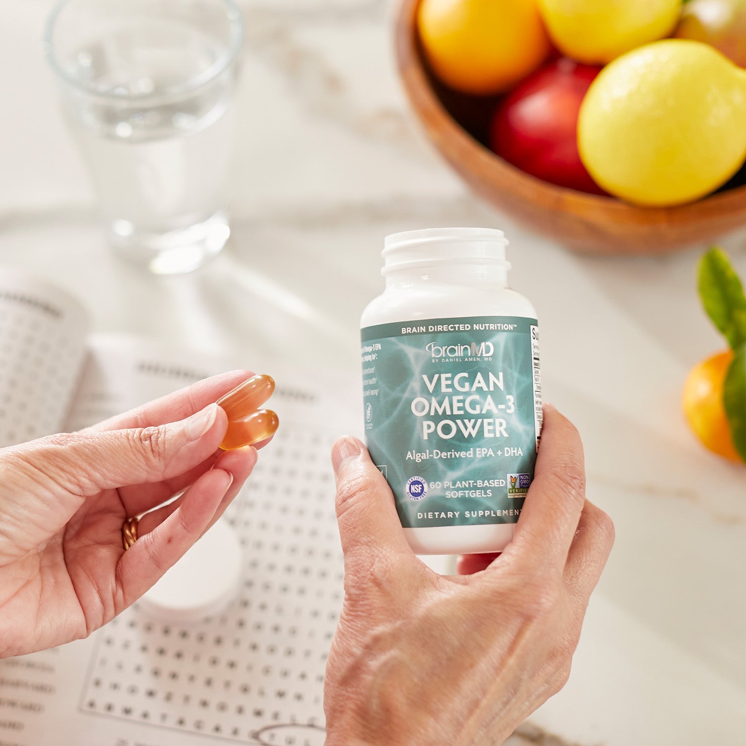 BrainMD Vegan Omega-3 Power: person holding softgels in one hand and a green supplement bottle in the other