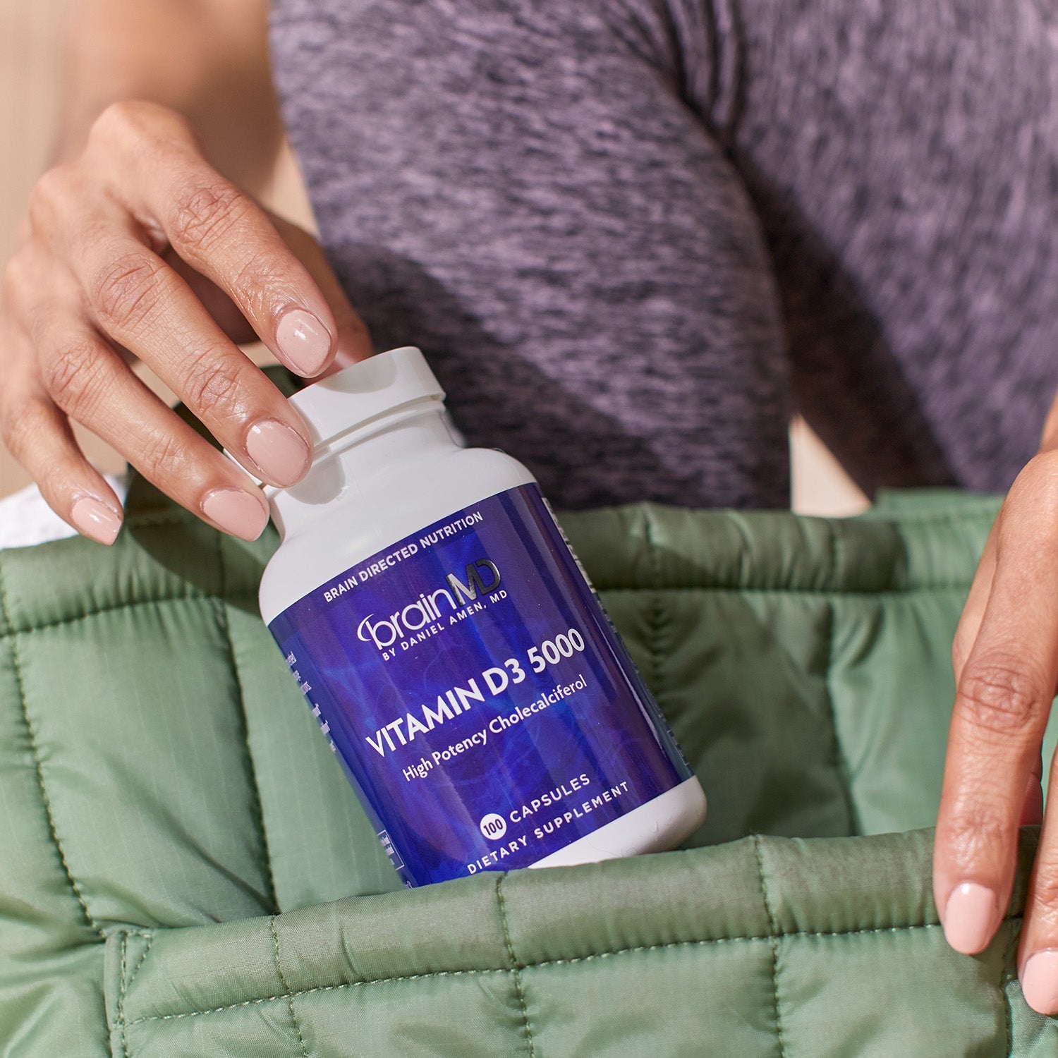 BrainMD Vitamin D3 5000: woman putting a purple supplement bottle into a green carry bag