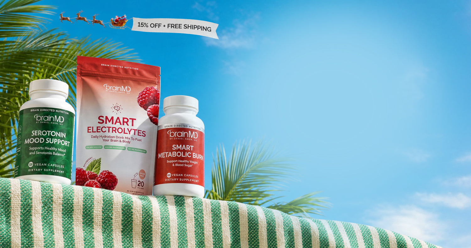 Three OrianMD wellness supplement products displayed on a green-and-white striped towel outdoors under a bright blue sky with palm leaves. The products are: a green bottle labeled 'Selenium Mood Support,' a red-and-white pouch labeled 'Smart Electrolytes,' and a red bottle labeled 'Smart Metabolic Balance.