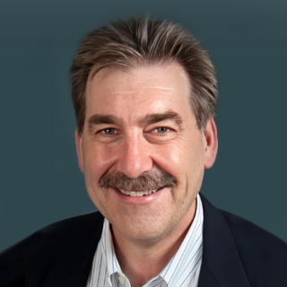 Dr. Earl Henslin wearing a dark jacket over a striped shirt on a blue background