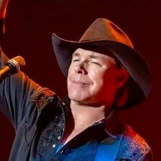 Michael Peterson country music star playing guitar with a raised fist on a stage with red lighting