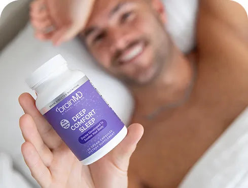 Man in bed holding up a purple sleep supplement bottle.