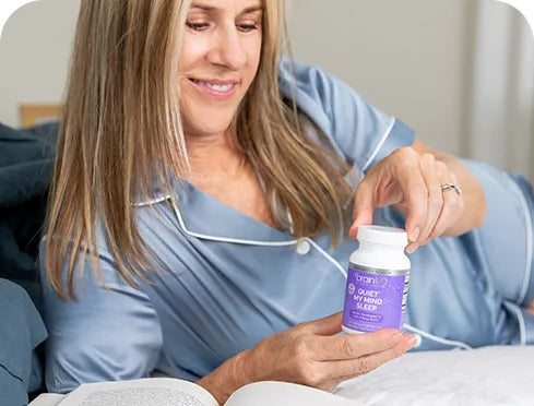 Woman in bed holding a purple sleep supplement bottle.