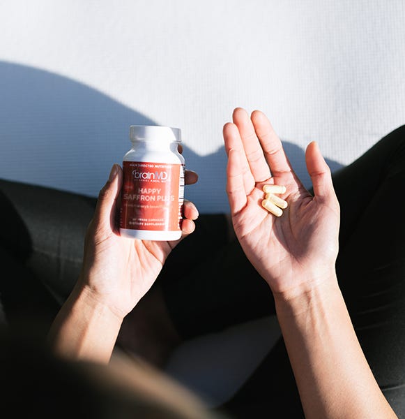 Person holding Happy Saffron Plus bottle and capsules, showcasing the best natural supplement for mood support and emotional wellness.