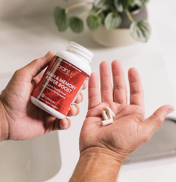  Hand holding daily serving of Brain & Memory Power Boost capsules next to the bottle