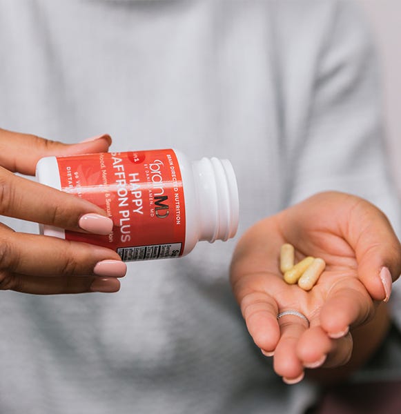 Lifestyle shot of a woman pouring award winning Happy Saffron Plus capsules into her hand, showcasing ease of use and natural mood support.